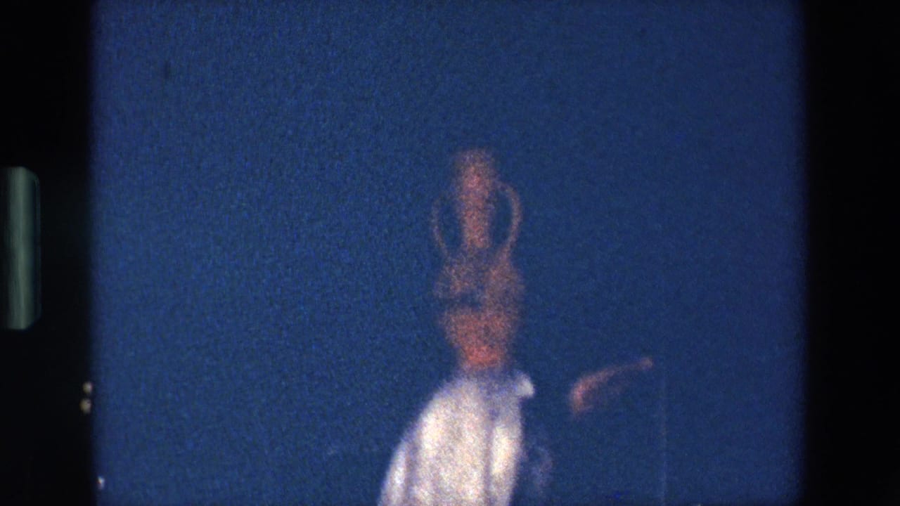 Blurred dancer in white costume with an amphora on her head against a dark blue stage.