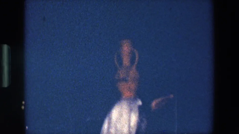 A softly focused frame shows the Palermo stage dancer turning or moving with the amphora still balanced on her head under dim blue lighting.