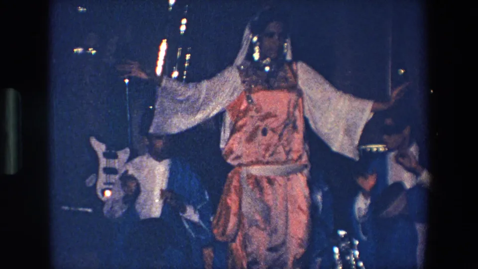 The 1967 Palermo scene shows the performer centered in a pink and white costume, with a guitarist and seated figures partly visible in the dim background.