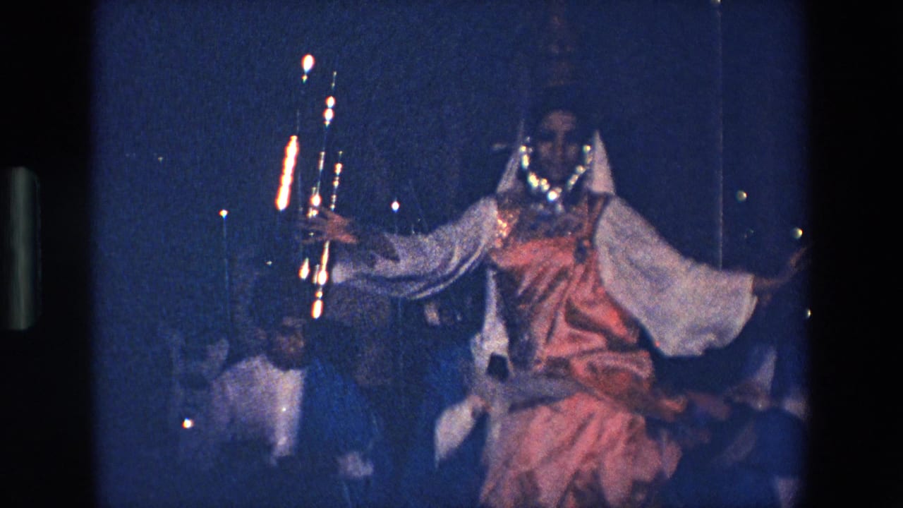 In Palermo, Italy in 1967, a woman in pink and white traditional Indian attire dances with arms extended while seated male musicians appear behind her in low blue light.