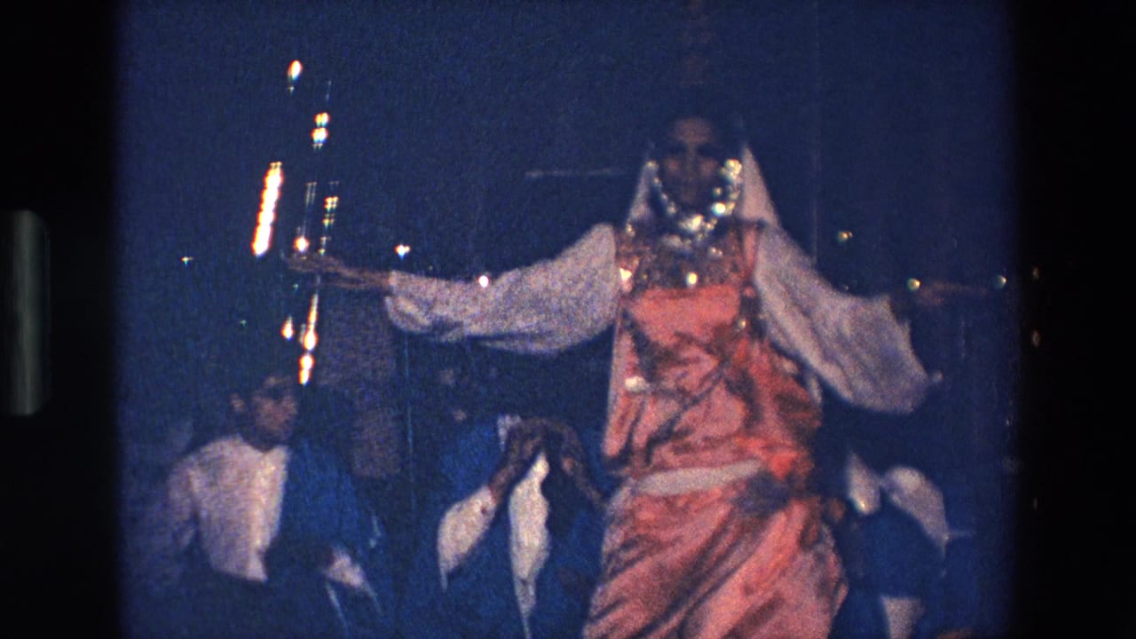 Dancer faces forward with one arm extended as musicians sit in the background.