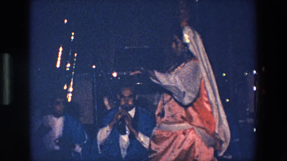 The final frame shows the dancer in profile with a raised hand and trailing veil, while suited male musicians and instruments remain visible in the dim background.