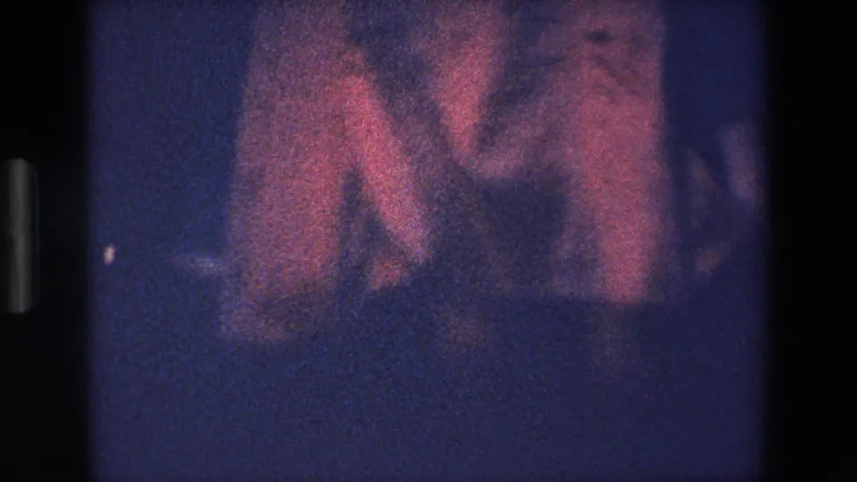 1967 Palermo home-movie frame showing a woman’s feet near the ground with pink fabric moving around her legs under blue-purple night exposure.