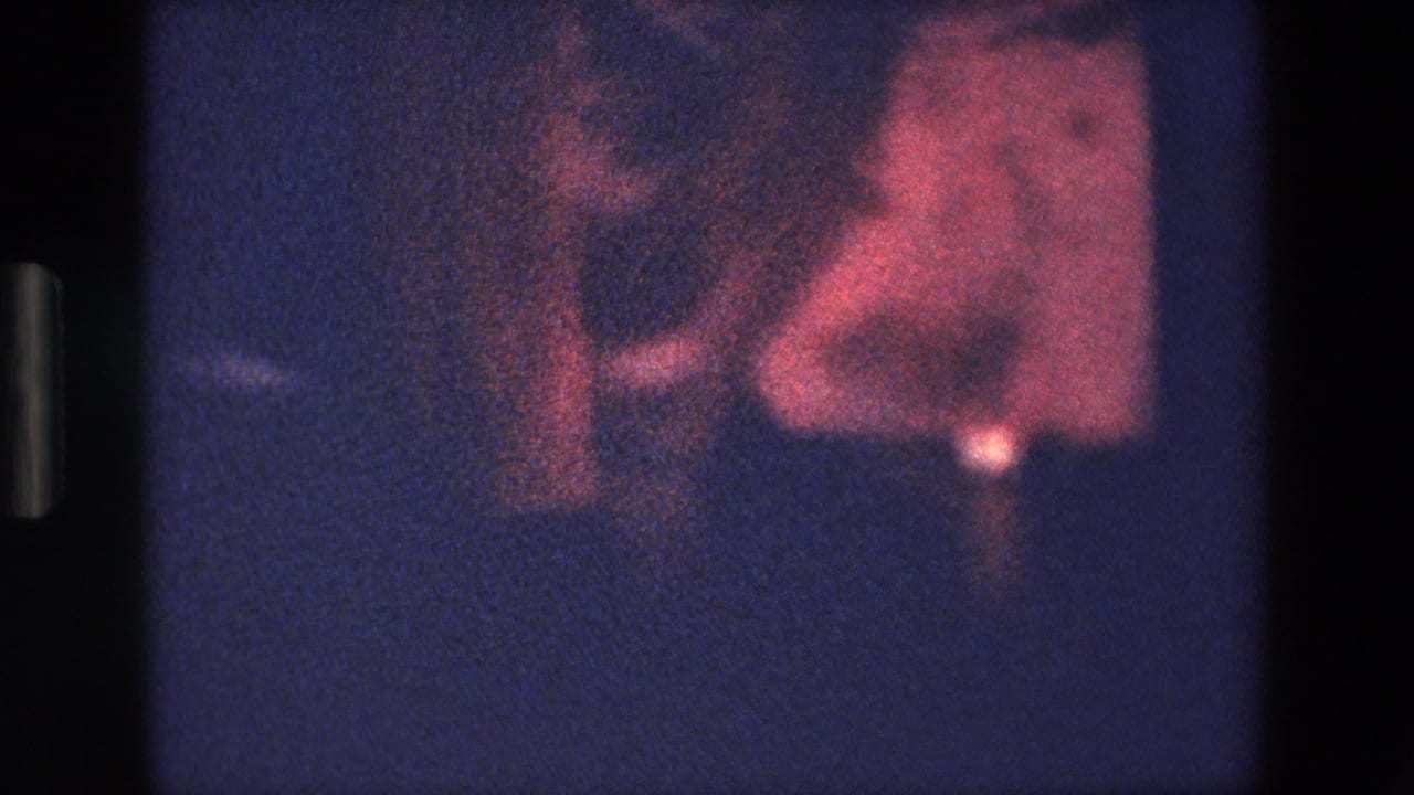 1967 Palermo home-movie frame with an indistinct red-toned moving figure or fabric area against deep blue shadows and visible film borders.