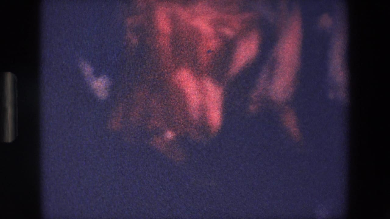 Blurred red and dark shapes inside a grainy film frame.