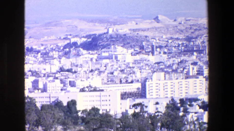 A bright 1967 Palermo city panorama shows rows of buildings, dark foreground trees, and pale hills beyond, with aged color and soft 8mm detail.