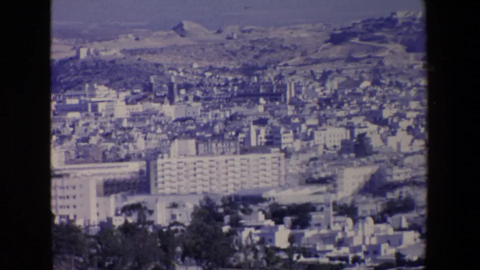1967 Palermo panorama on 8mm film, with apartment blocks and dense pale urban buildings set below sunlit hills.