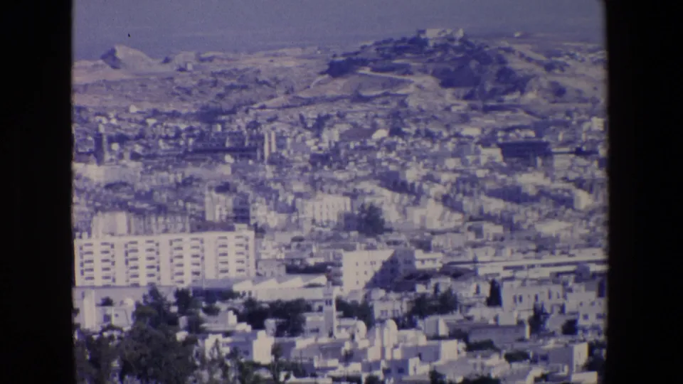 1967 Palermo home-movie frame showing a dense urban foreground, larger residential blocks, and hillside development under a hazy sky.