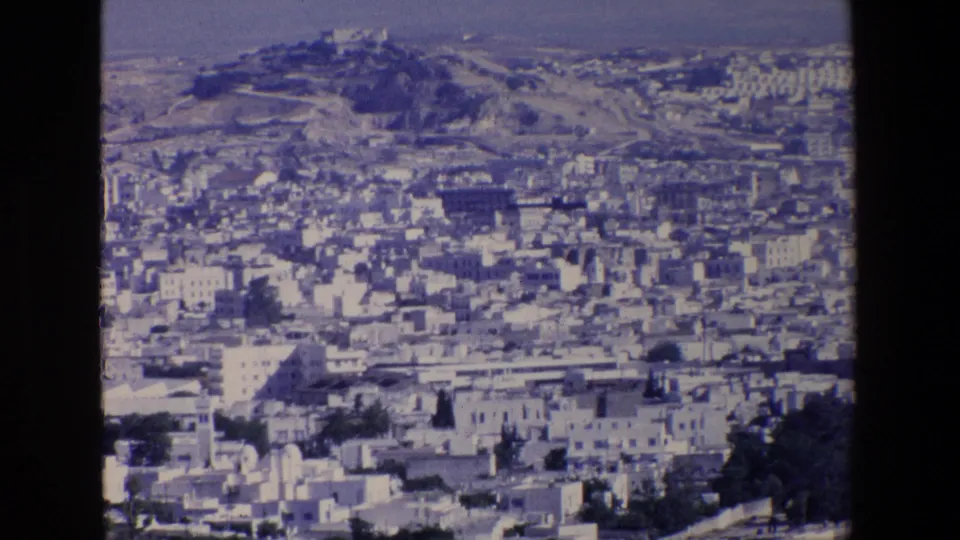 1967 8mm home-movie frame showing Palermo from above, with tightly packed pale buildings, a distant hilltop landmark, and soft blue film color.