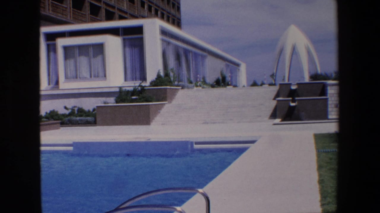 Blue swimming pool beside a white hotel terrace and sculptural architectural feature.
