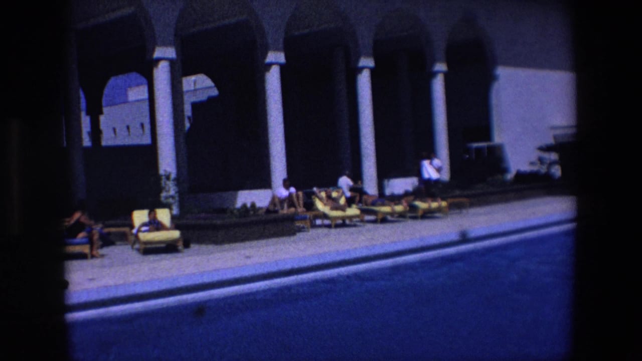 Guests sit and recline on yellow and blue poolside chairs beneath tall white pillars at a Palermo resort in 1967.