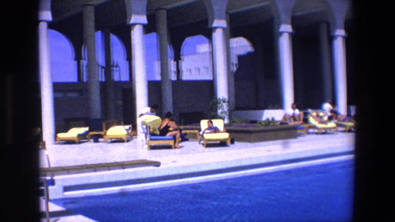 Poolside patio with lounge chairs, columns, and people in swimwear.