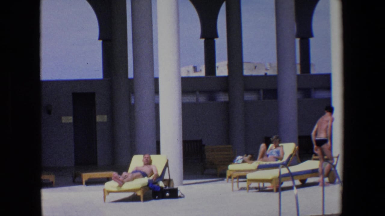 Wide 1967 Palermo poolside home-movie frame showing a shirtless man in a blue swimsuit reclining on a yellow lounge chair beneath white columns, with other visitors sunbathing nearby.