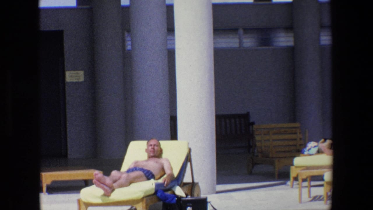 Closer poolside view of a shirtless man reclining on a yellow lounge chair near white columns.