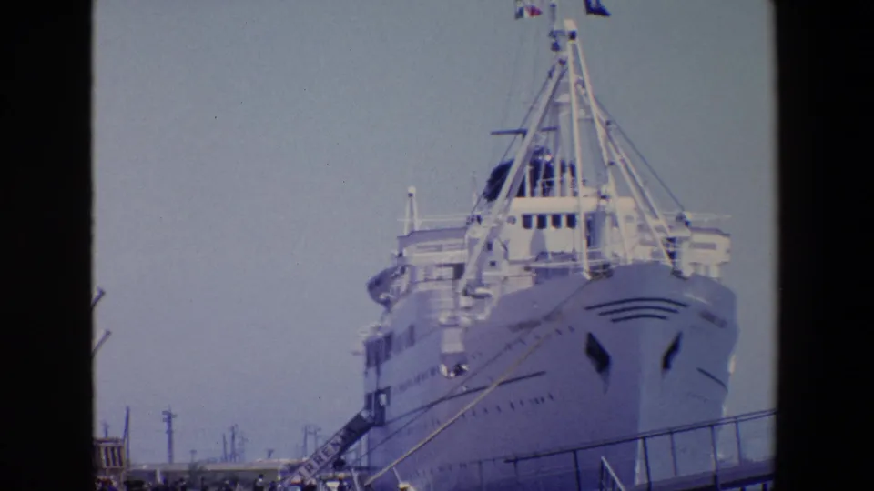 Home-movie frame from Palermo in 1967 showing the front of a large white passenger ship, its upper decks, gangway, and pier railings under a pale sky.