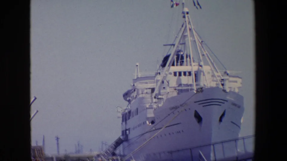 1967 Palermo travel frame showing a large docked passenger ship from a low pier angle, with gangway access, railing lines, and distant people at the waterfront.