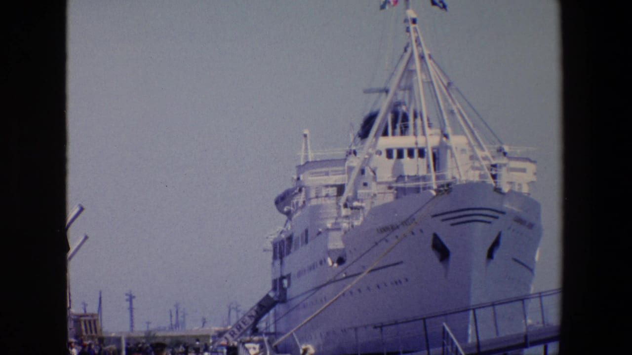 1967 Palermo 8mm frame showing a large white passenger ship at the pier with rigging, gangway lines, utility poles, and people gathered along the dock.