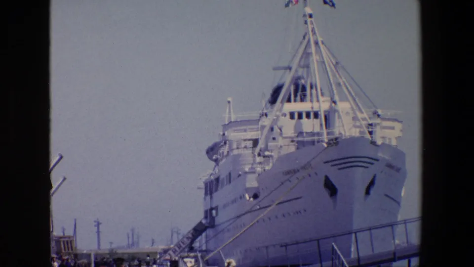 1967 Palermo 8mm frame showing a large white passenger ship at the pier with rigging, gangway lines, utility poles, and people gathered along the dock.