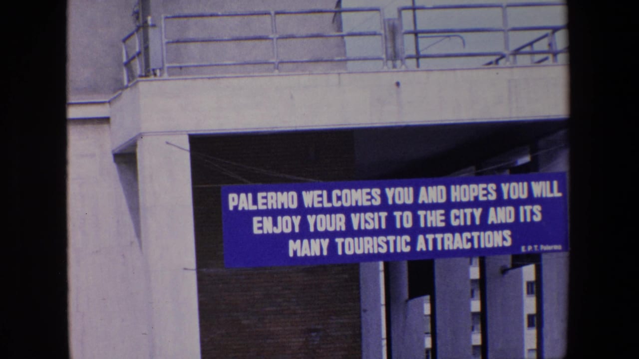 A blue Palermo tourist welcome sign appears under concrete urban infrastructure in this 1967 8mm frame.