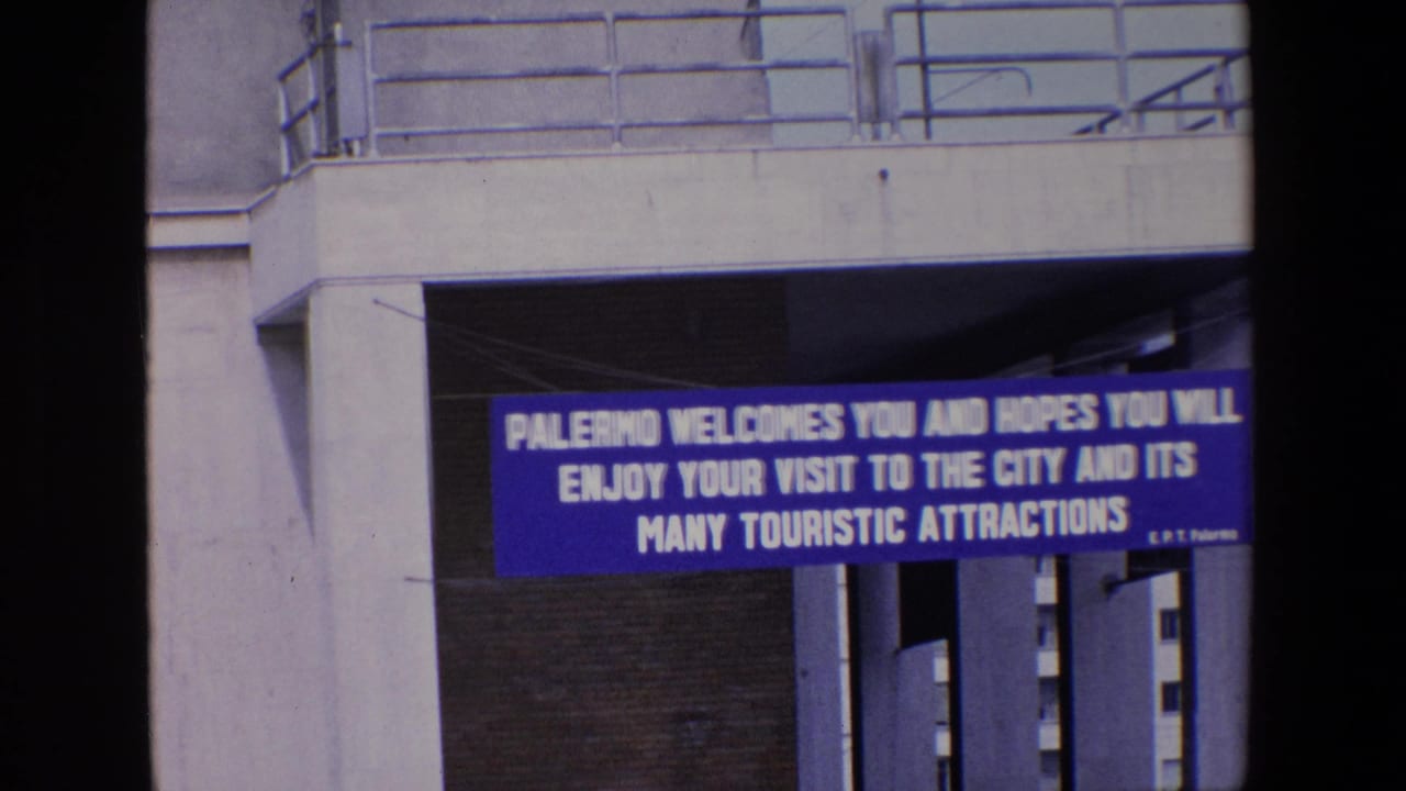 The Palermo welcome banner remains centered below the overpass, with 8mm softness and saturated blue color visible in the frame.