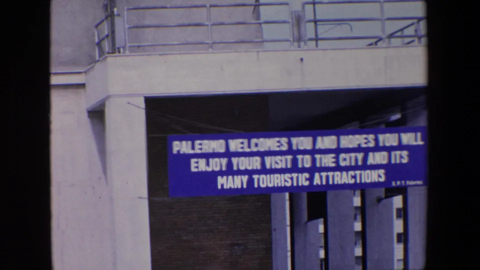 The Palermo welcome banner remains centered below the overpass, with 8mm softness and saturated blue color visible in the frame.