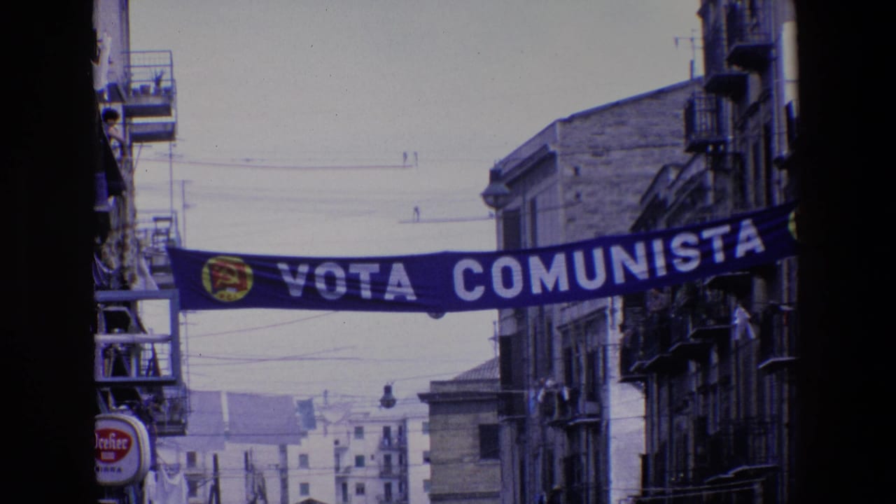 The political street banner reading Vota Comunista crosses between buildings in Palermo, with apartment balconies and overhead wires framing the 1967 street view.
