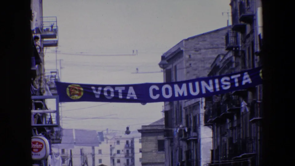 The political street banner reading Vota Comunista crosses between buildings in Palermo, with apartment balconies and overhead wires framing the 1967 street view.
