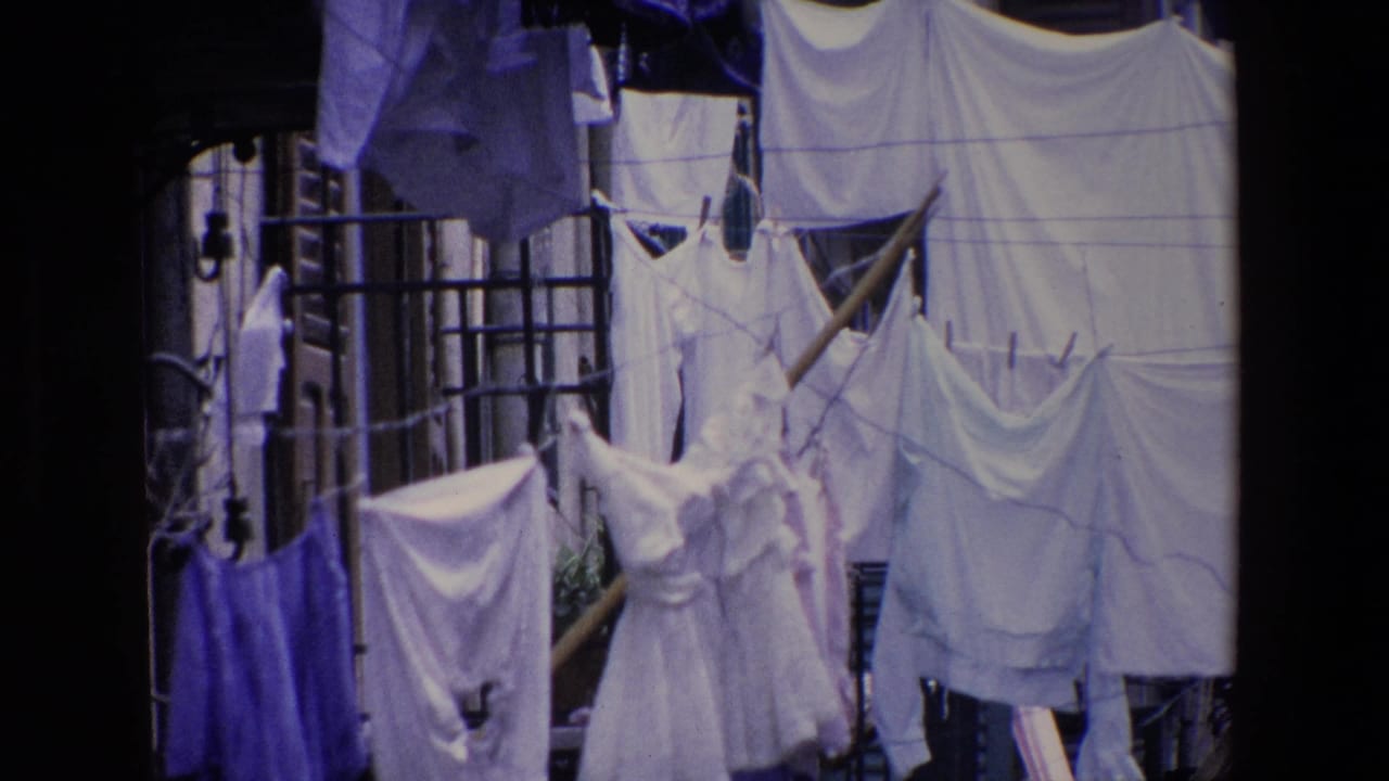 A closer 1967 home-movie view of outdoor laundry in Palermo, with pale garments and sheets layered across lines between building edges.