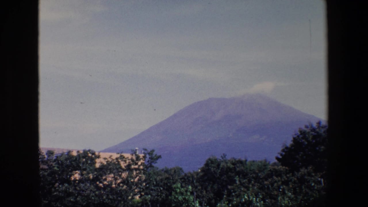 Distant mountain with a faint cloud near the summit, seen above trees and light rooftops.