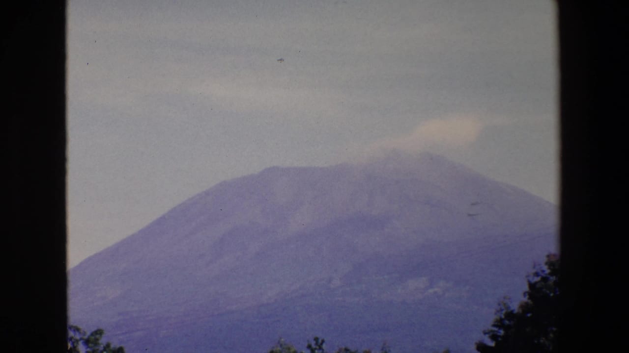 1967 Palermo 8mm frame showing a distant broad mountain with a faint pale plume near the summit, viewed through dark vertical window framing.