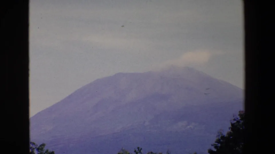 1967 Palermo 8mm frame showing a distant broad mountain with a faint pale plume near the summit, viewed through dark vertical window framing.