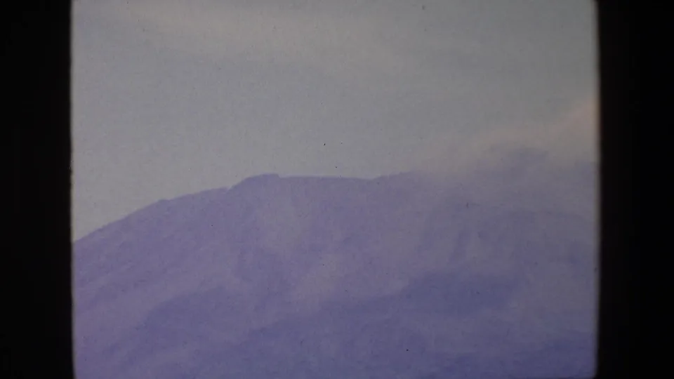 1967 Palermo home-movie frame showing a hazy mountain ridge with a pale plume or cloud near the summit and dark framing at the edge.