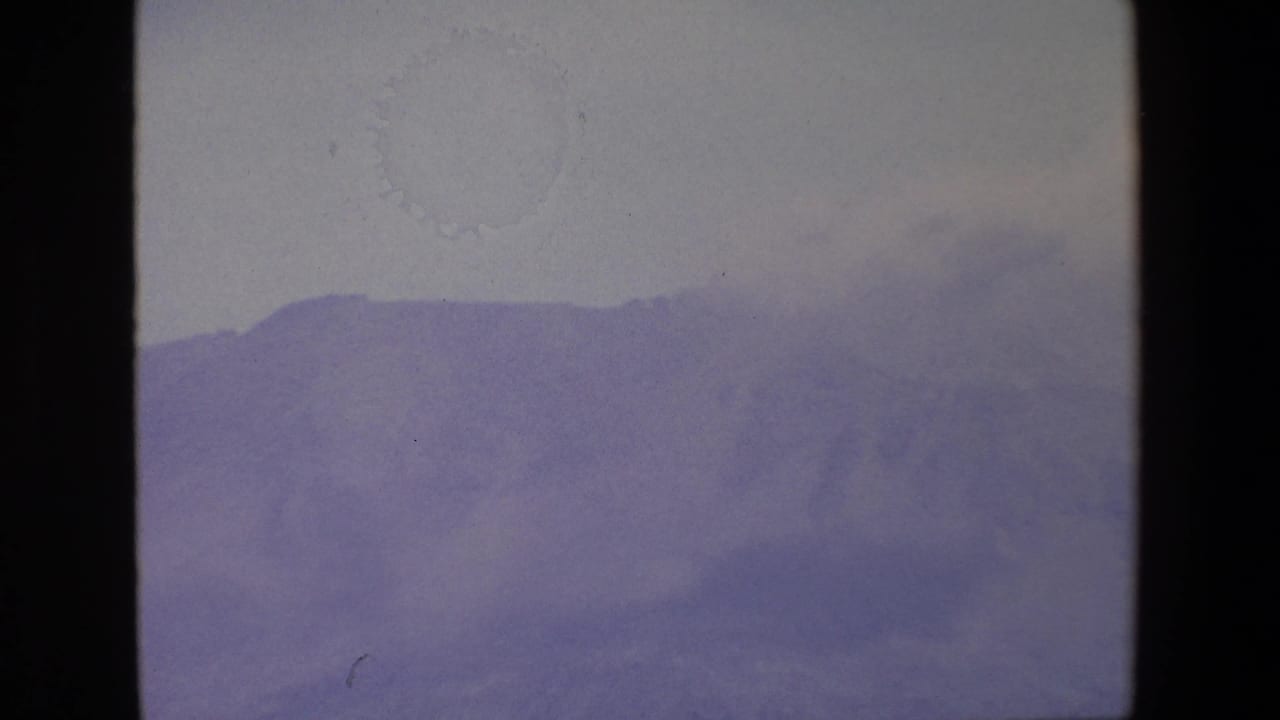 1967 Palermo-area 8mm frame showing a distant mountain ridge softened by fog beneath a pale gray sky.