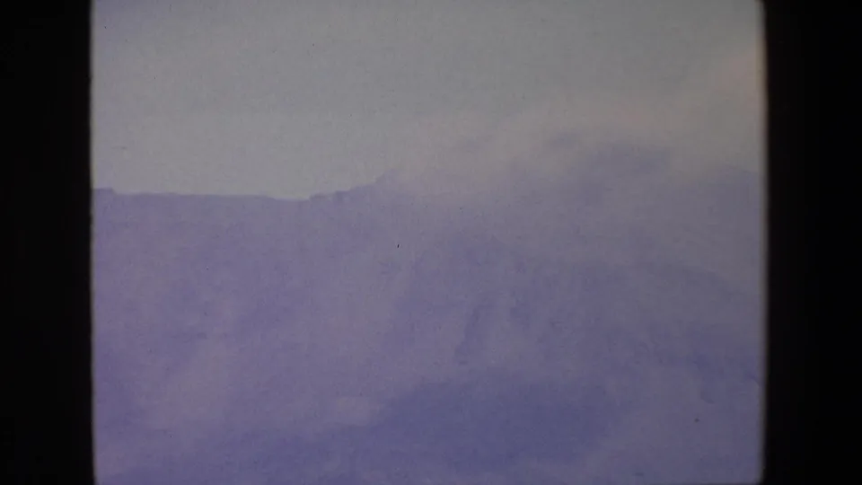 1967 Palermo-area 8mm frame of a broad, hazy mountain range with subdued purple-gray terrain and no visible people or structures.