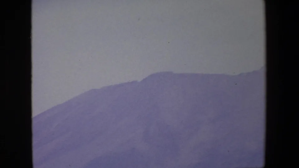1967 Palermo home-movie frame showing a hazy blue-purple mountain slope viewed through a dark window frame under a pale sky.