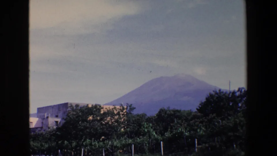 1967 Palermo 8mm frame showing a mountain peak beyond trees and a low building, with dark window framing at the sides.