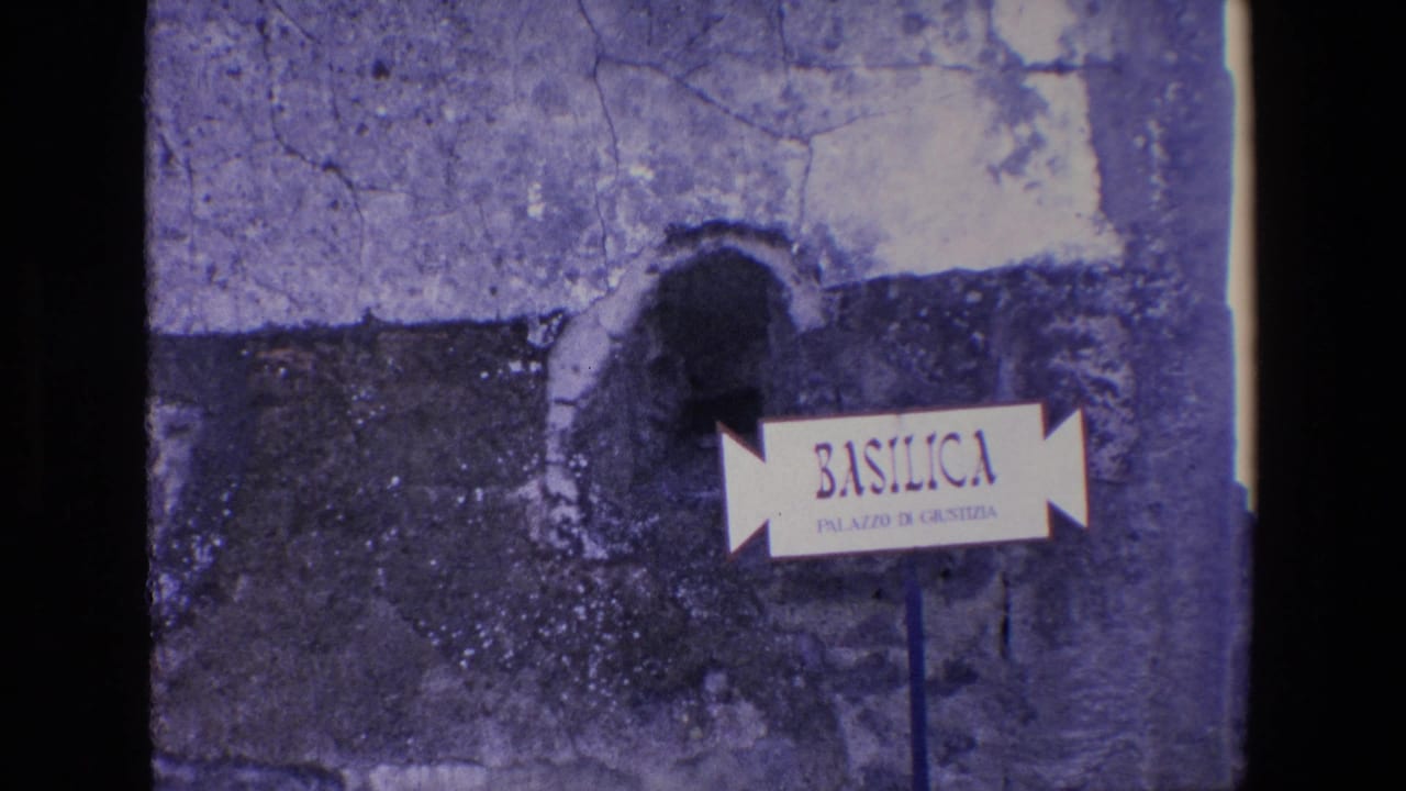 Directional Basilica sign in front of a worn stone wall and dark arched opening.