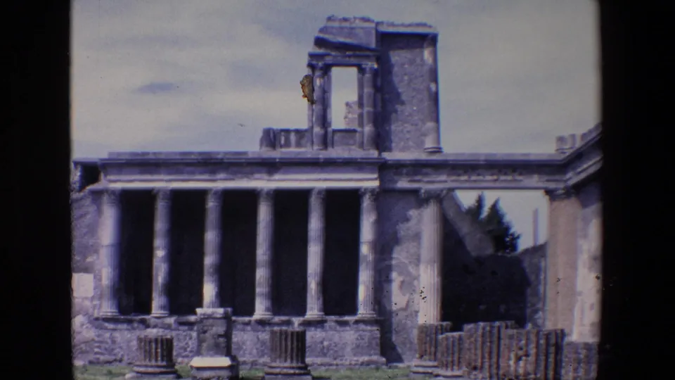 1967 Palermo 8mm frame showing a closer visitor-shot view of tall columns, roofline remains, an upper stone section, grass, and loose architectural fragments.