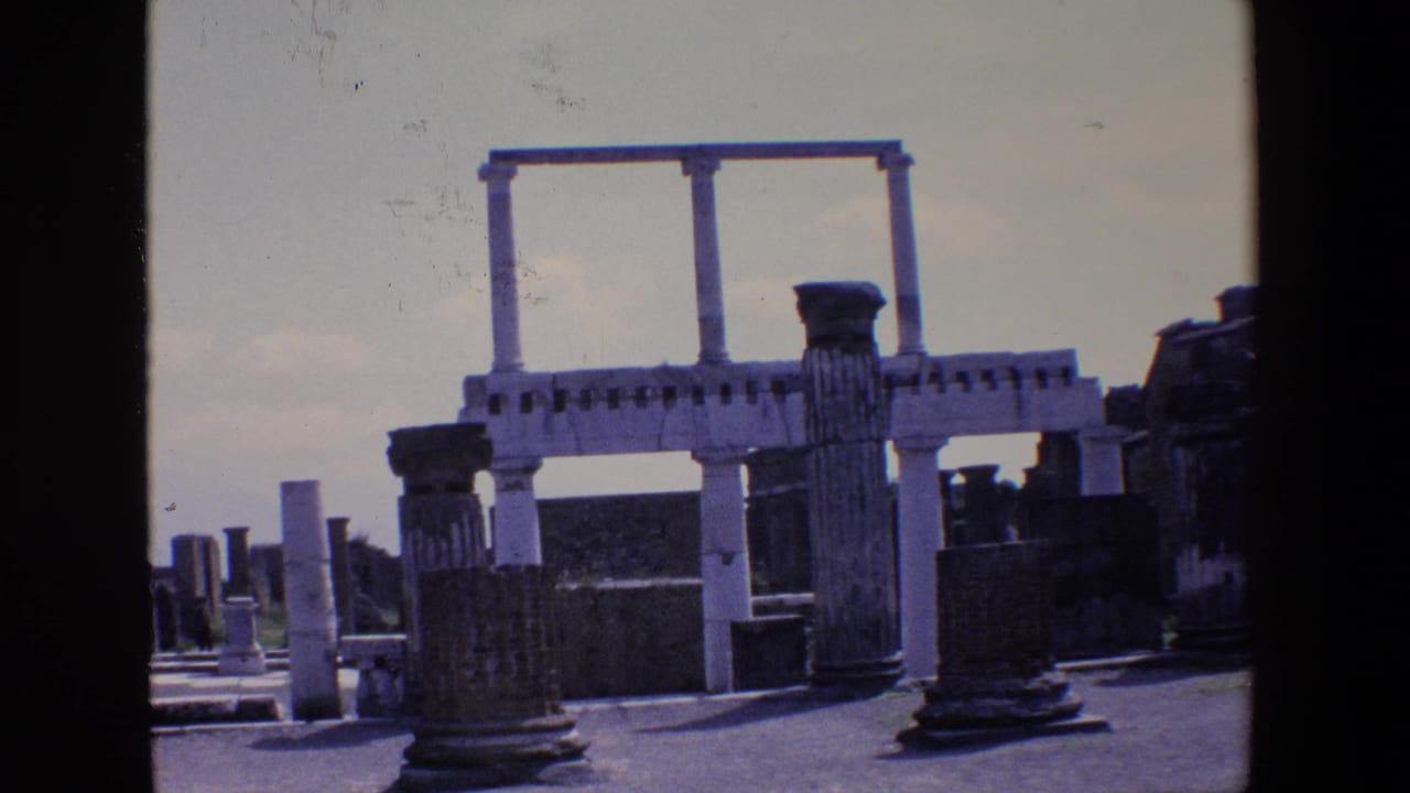 1967 Palermo, Italy home-movie frame showing weathered stone columns, low ruin walls, and a pale overhead architectural structure against a bright sky.