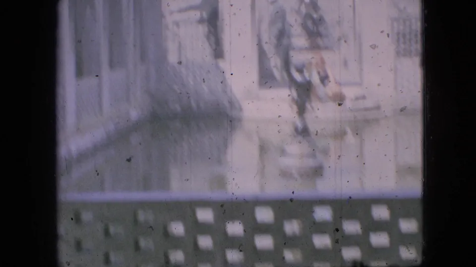 Faded 1968 Branson, Missouri home-movie frame showing a sunlit fountain area with pale masonry, decorative lattice, reflective water, and indistinct people near the basin.