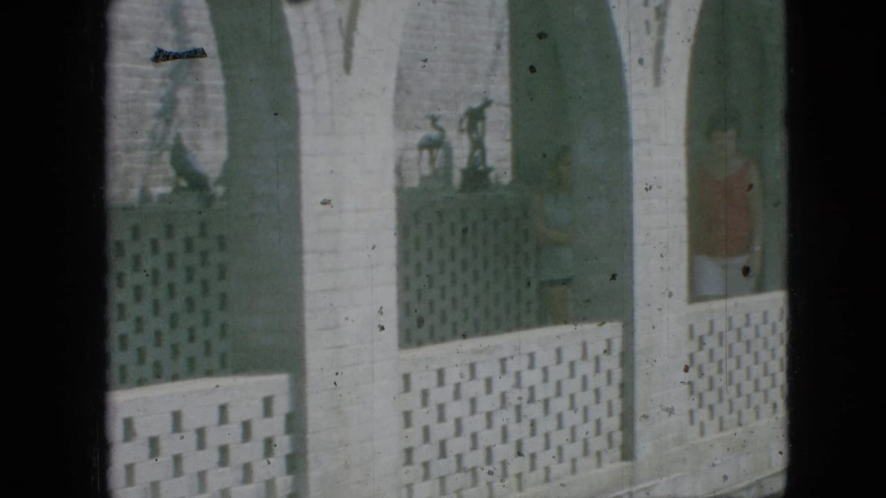 1968 Branson, Missouri 8mm frame showing a white arched courtyard wall with patterned lattice blocks and distant concrete figures under soft, green-tinted exposure.