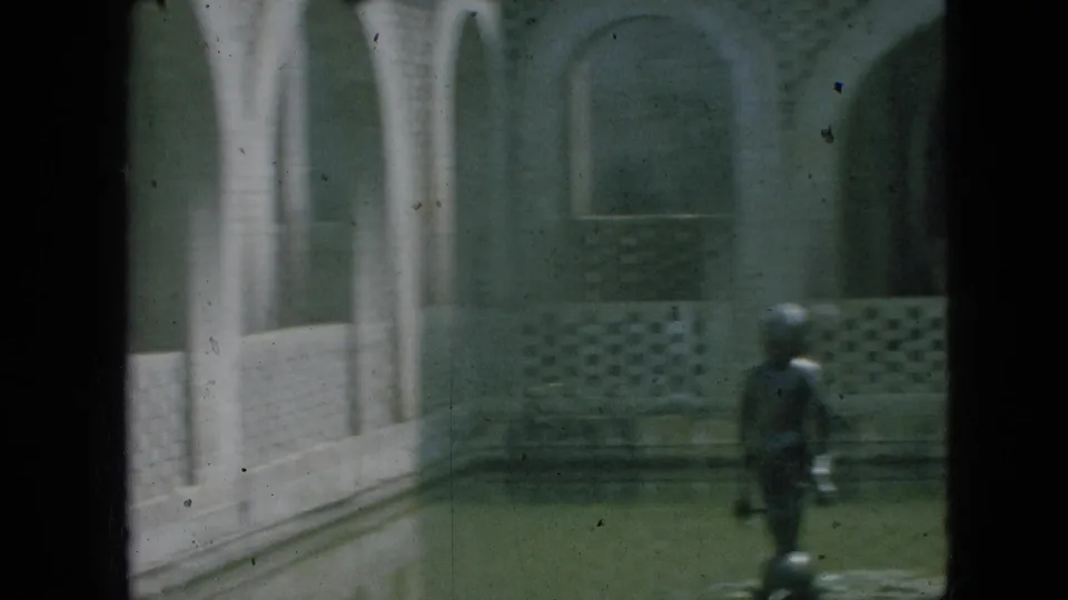 1968 Branson, Missouri home-movie frame of a white masonry courtyard with arched openings, patterned walls, a distant person, and sculptural figures.