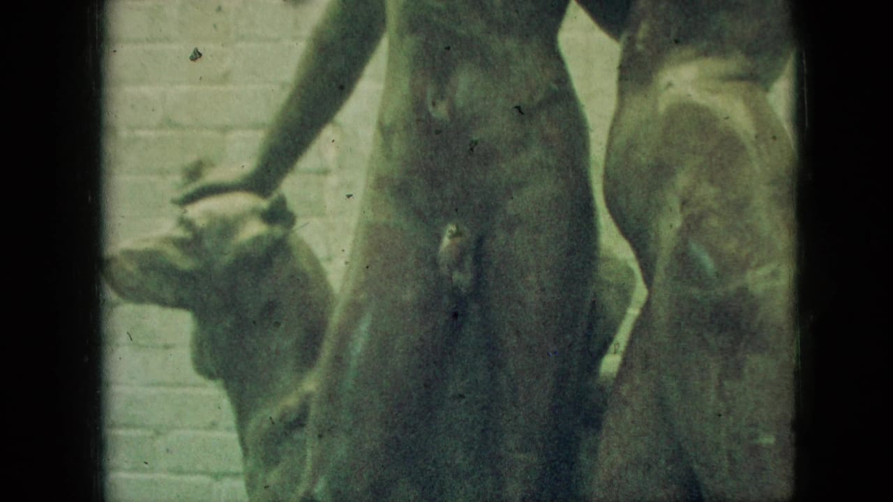 Close 1968 Branson home-movie view of the Adam and Eve sculpture, showing nude figures and a dog form against a brick wall with soft faded 8mm color.
