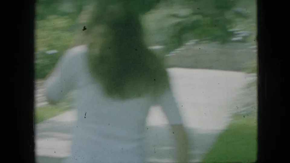 A heavily blurred 8mm frame shows a person in a light dress moving near a paved walkway, with lawn and trees in the surrounding Branson park setting.