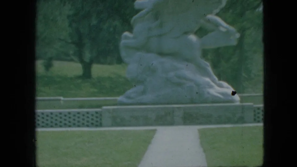 A white outdoor statue of intertwined figures on a pedestal stands beside a paved path and lawn in the 1968 Branson, Missouri park footage.