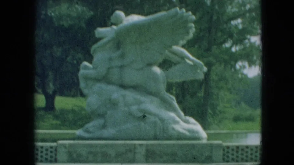 1968 Branson, Missouri frame with the winged sculpture filling more of the view, set against green trees and a low stone base.