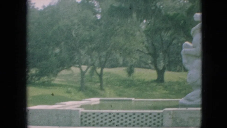 1968 Branson, Missouri frame where the sculpture is mostly at the right edge, leaving the landscaped lawn, trees, low wall, and walkway area visible.