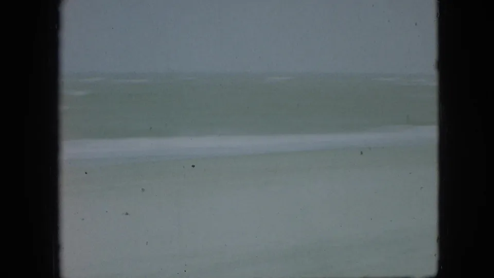 1968 8mm home-movie beach frame associated with Branson, Missouri, showing muted water and a low surf line beneath a hazy sky.