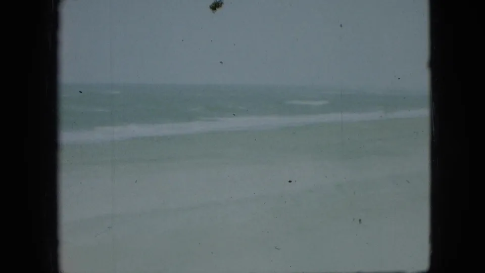 Faded 8mm shoreline frame from the stated 1968 Branson, Missouri clip, with pale water, a soft surf band, and visible dust and scratches.
