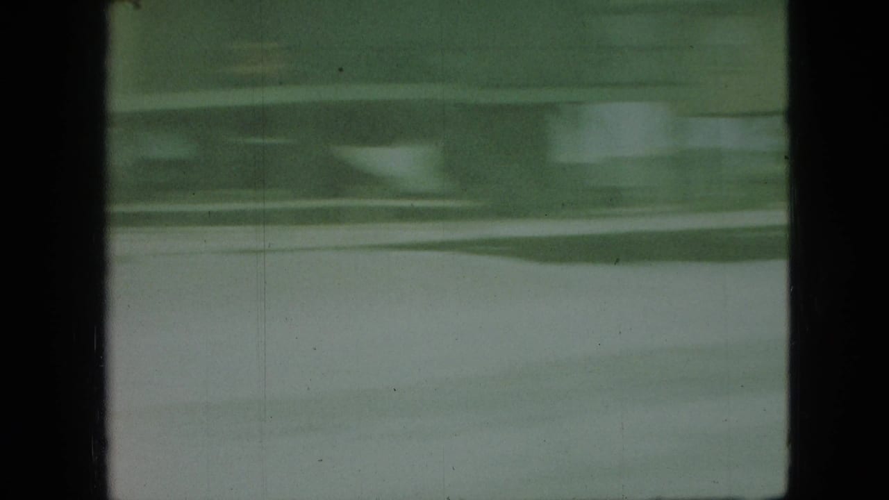 Green-tinted 8mm frame from the Branson vacation clip showing wavy water bands, dark borders, and soft handheld blur.